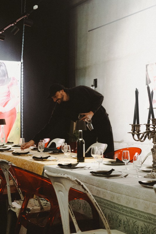 Un homme en noir dispose les verres sur la table, entre chandeliers et bouteilles