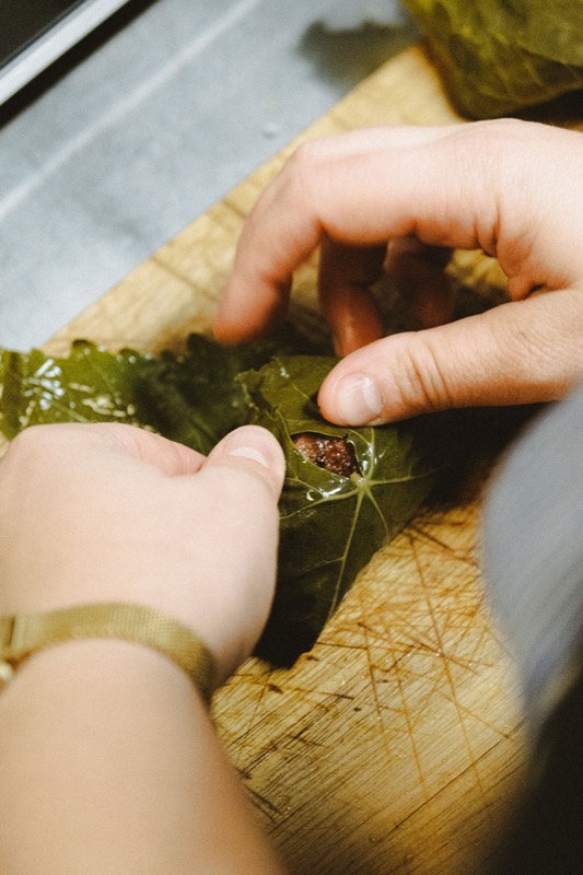 Des mains roulent une saucisse dans une feuille de vigne sur une planche