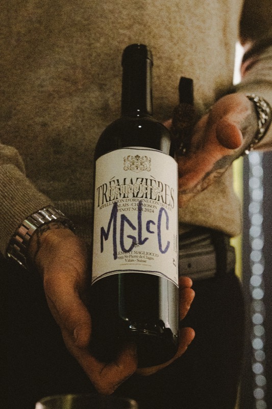 Une main tient une bouteille de vin rouge à l'étiquette blanche