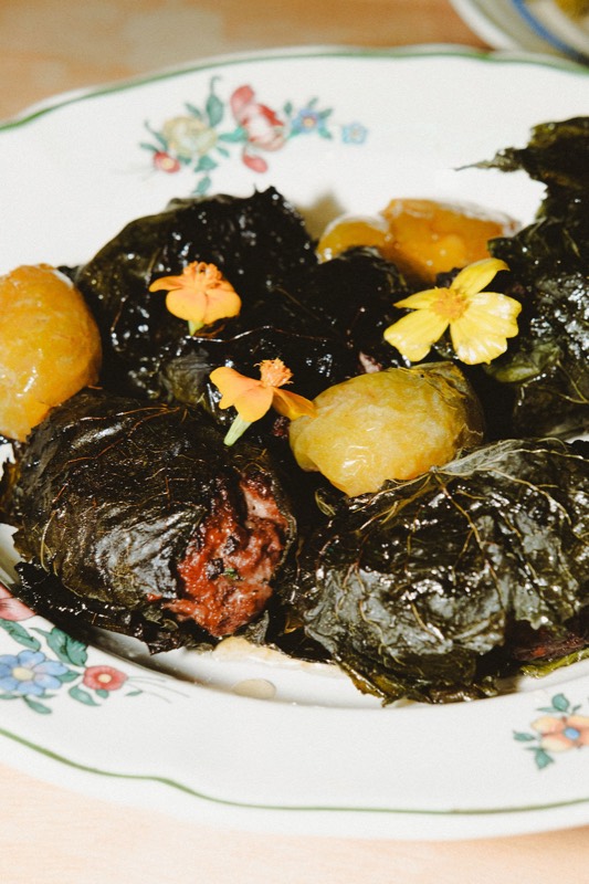 Saucisses en feuille de vigne, reines-claudes et fleurs jaunes sur une assiette fleurie