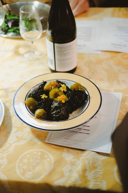 Une assiette de saucisses en feuille de vigne sur une nappe dorée, une bouteille et le menu imprimé à côté