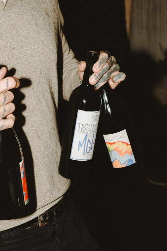 Deux bouteilles de vin tenues par des mains tatouées