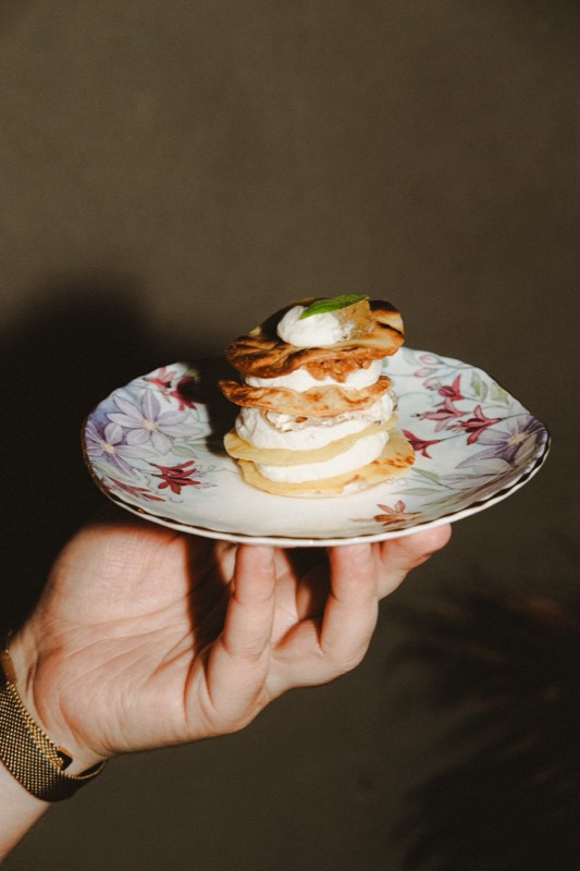Une main tient une assiette fleurie avec un mille-crêpes