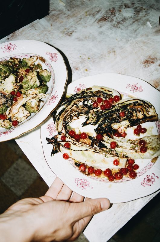 Un quartier de chou brûlé parsemé de groseilles rouges, et une salade de brocoli, sur des assiettes fleuries