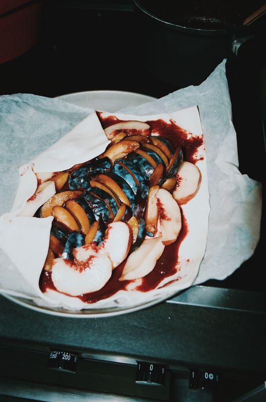Une galette aux prunes et aux pêches, crue, sur du papier cuisson