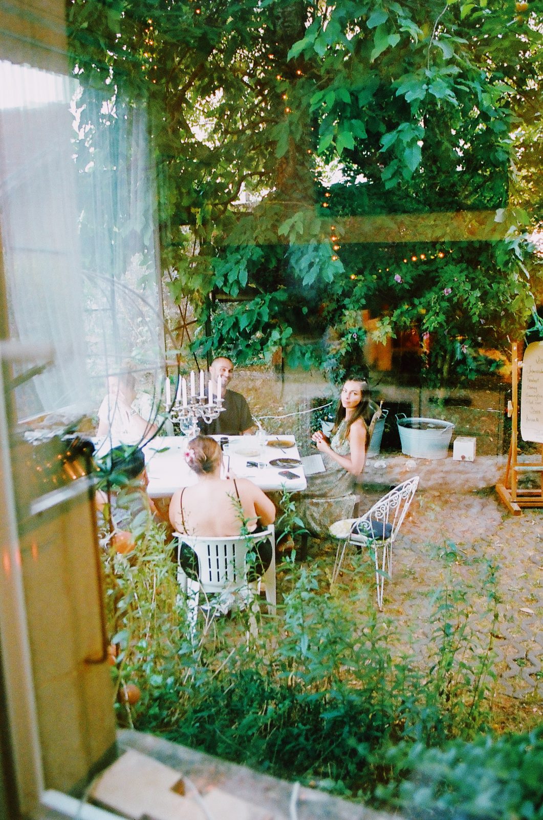 Le jardin de Cossonay vu depuis la cuisine : la grande table dressée sous les arbres, trois convives déjà assis