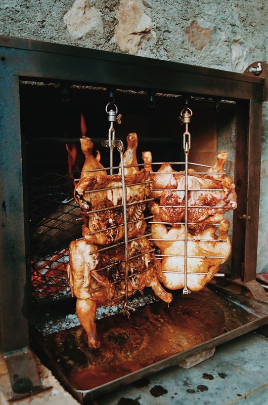Deux poulets suspendus dans des paniers devant le feu d'une cheminée en pierre