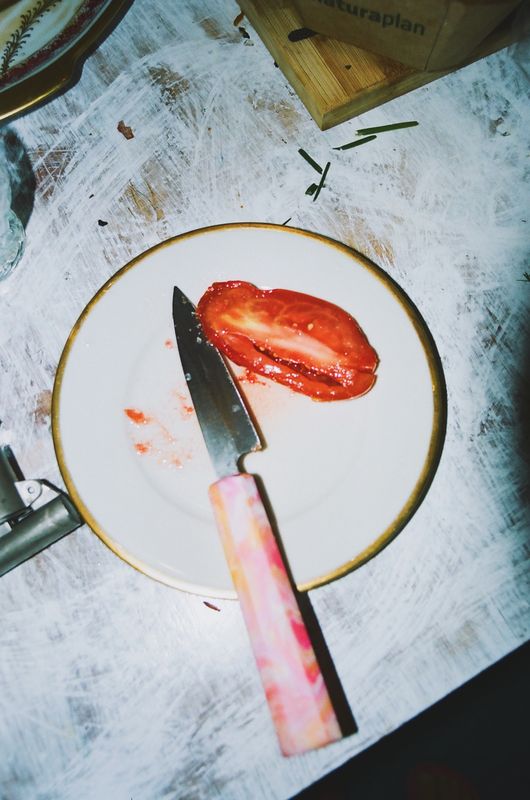 Une demi-tomate et un petit couteau au manche rose sur une assiette à liseré doré